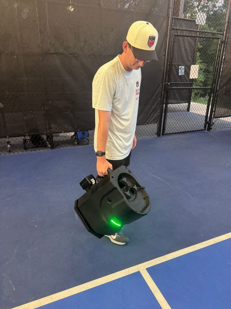 Coach Graham Richey carrying the Tennibot Partner Lite one-handed across a pickleball court