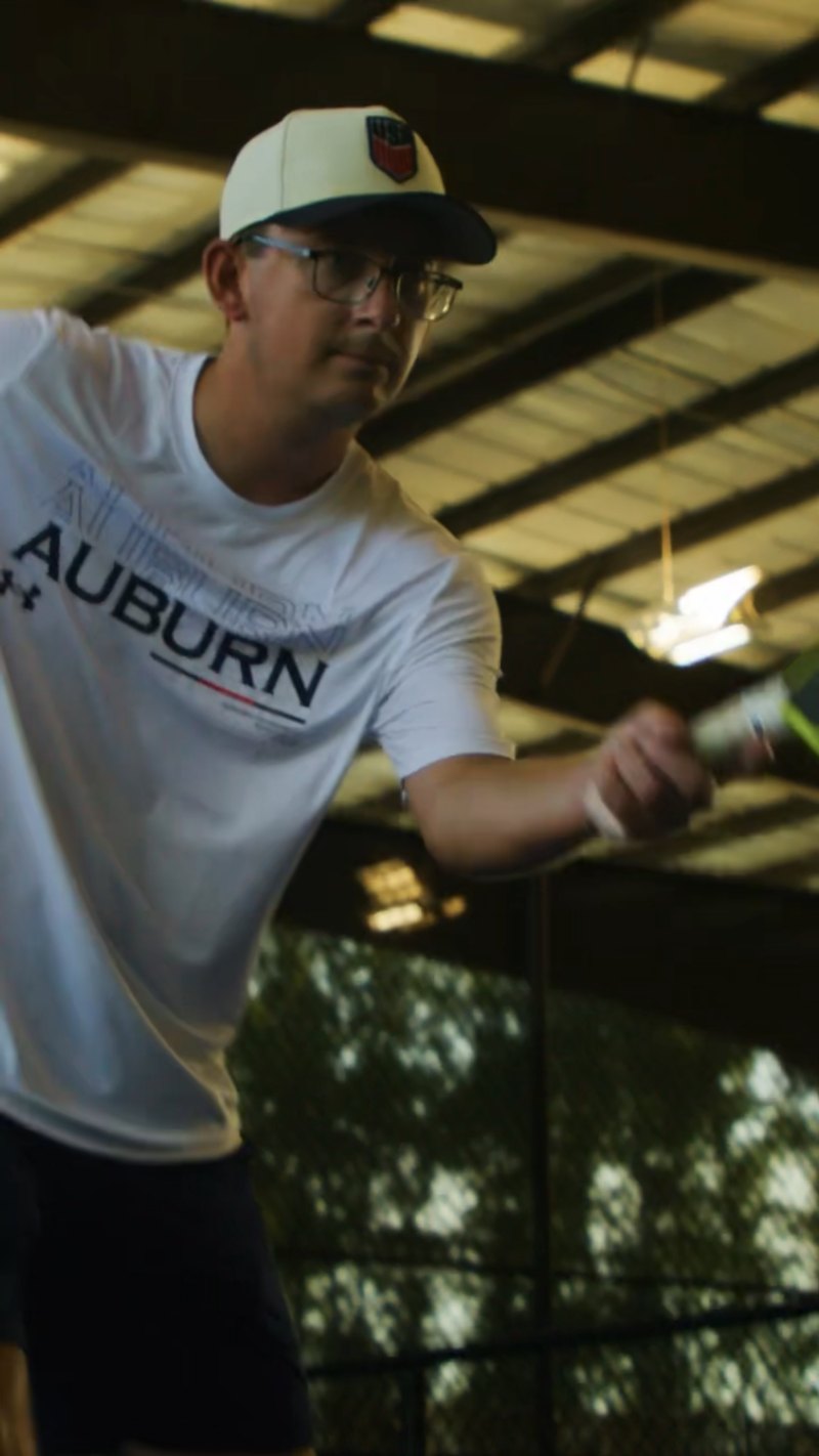 Coach Graham Richey hitting a pickleball during a drill against the Tennibot Partner Lite on a covered court